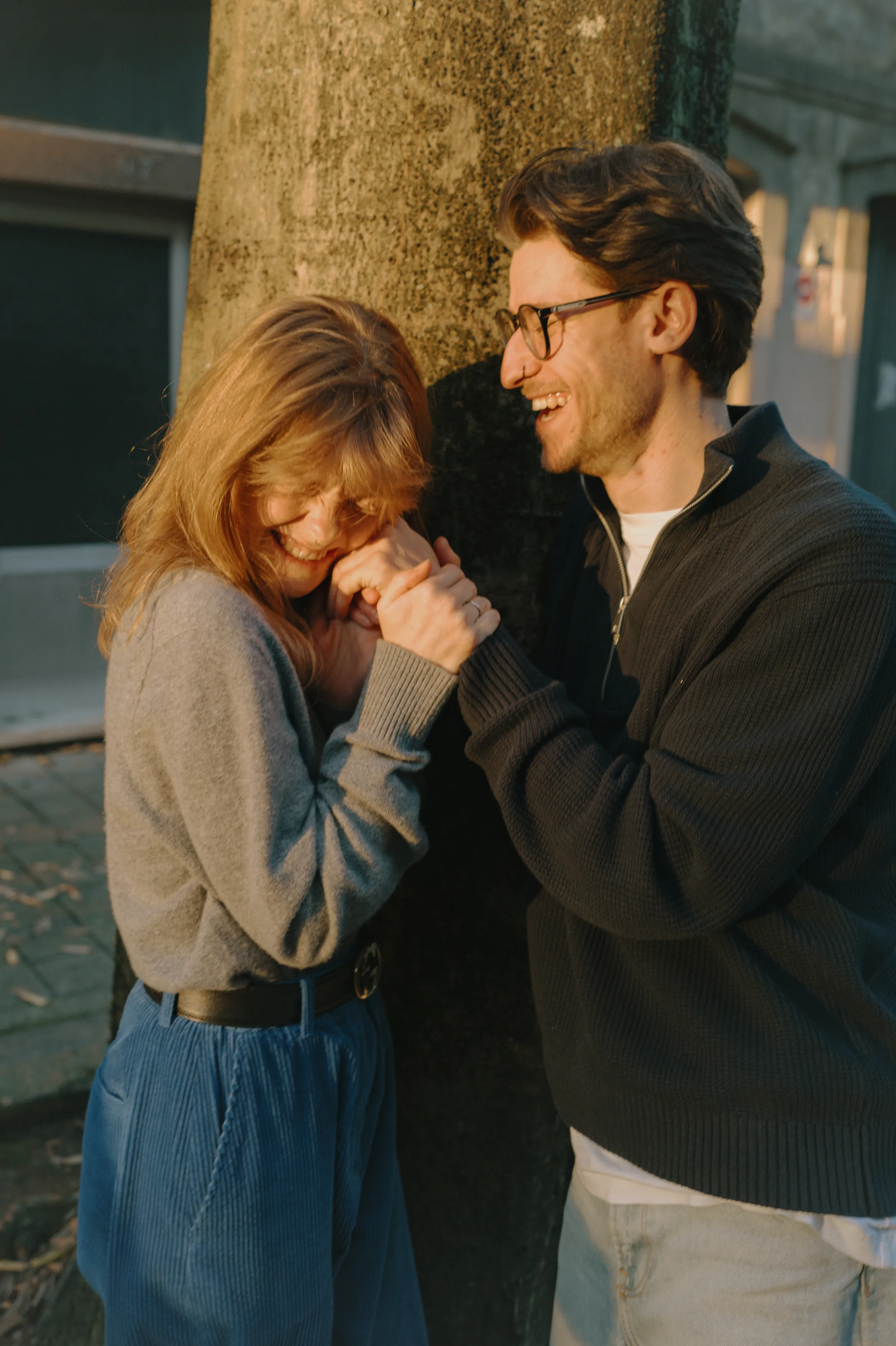 Couple portrait during an outdoor city walk, standing close by a tree in soft light