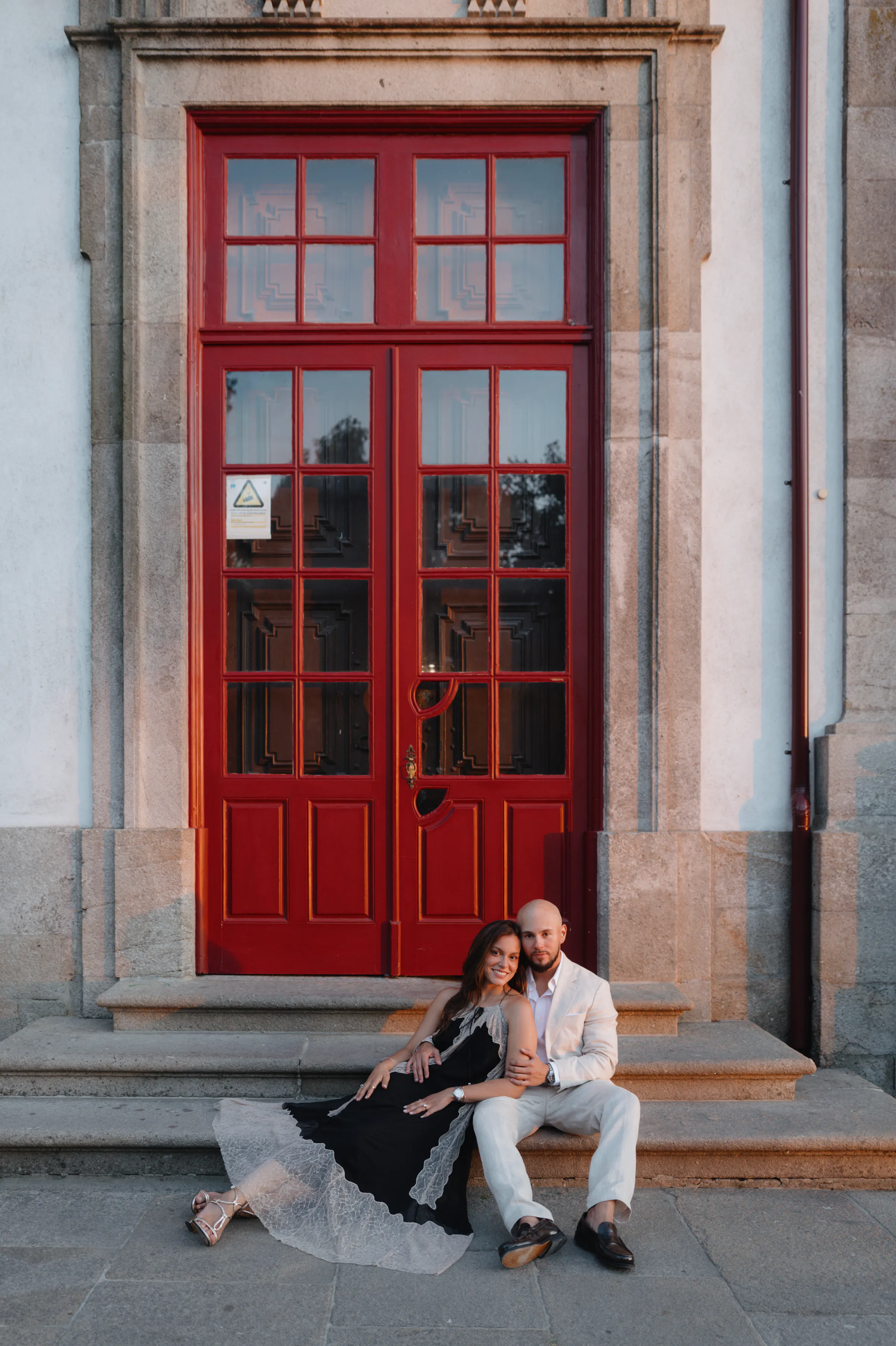 Couple portrait on stone steps before tall red doors during an outdoor city session.