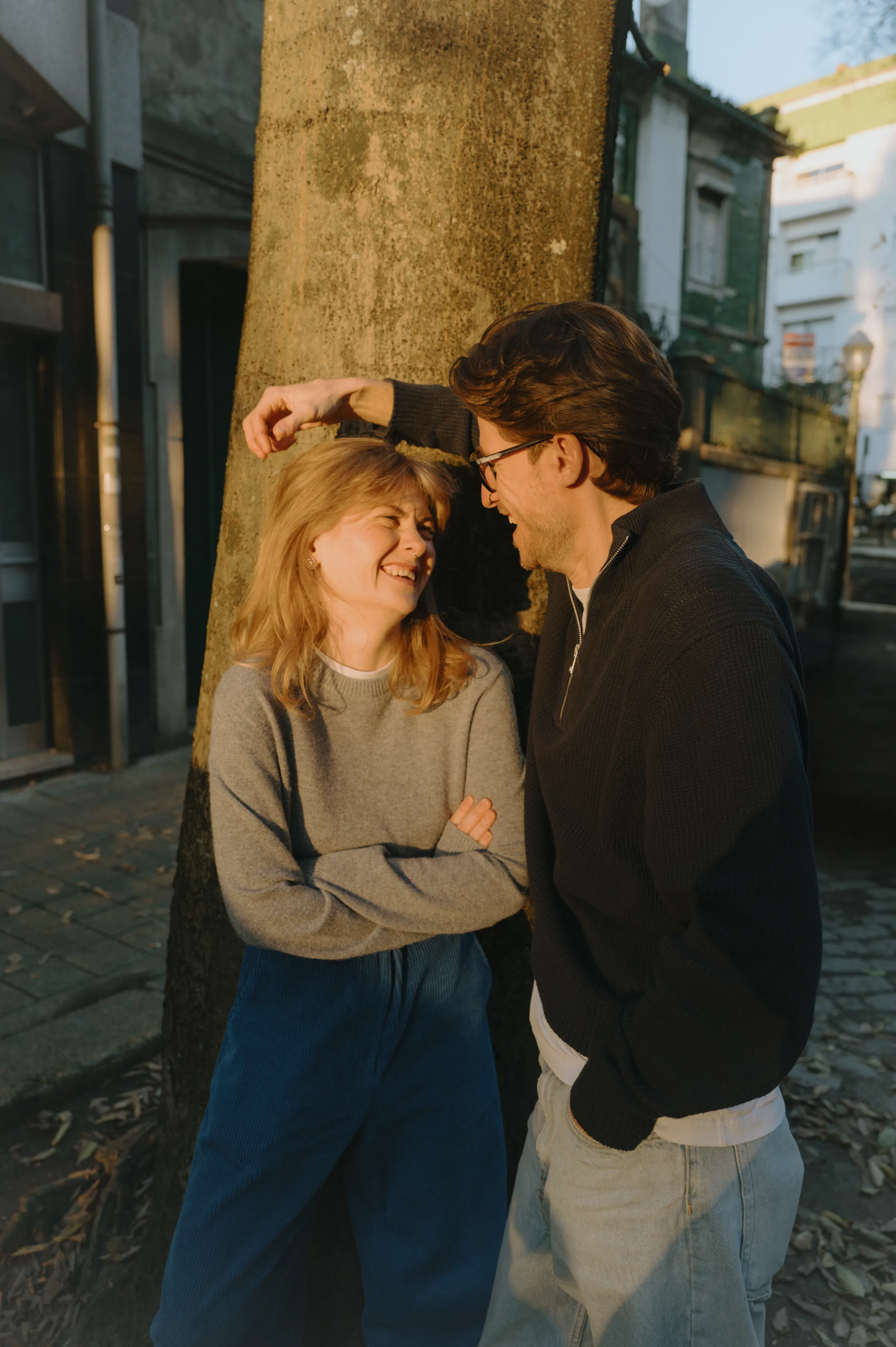 Couple portrait on a city street beside a tree, captured in warm soft light.