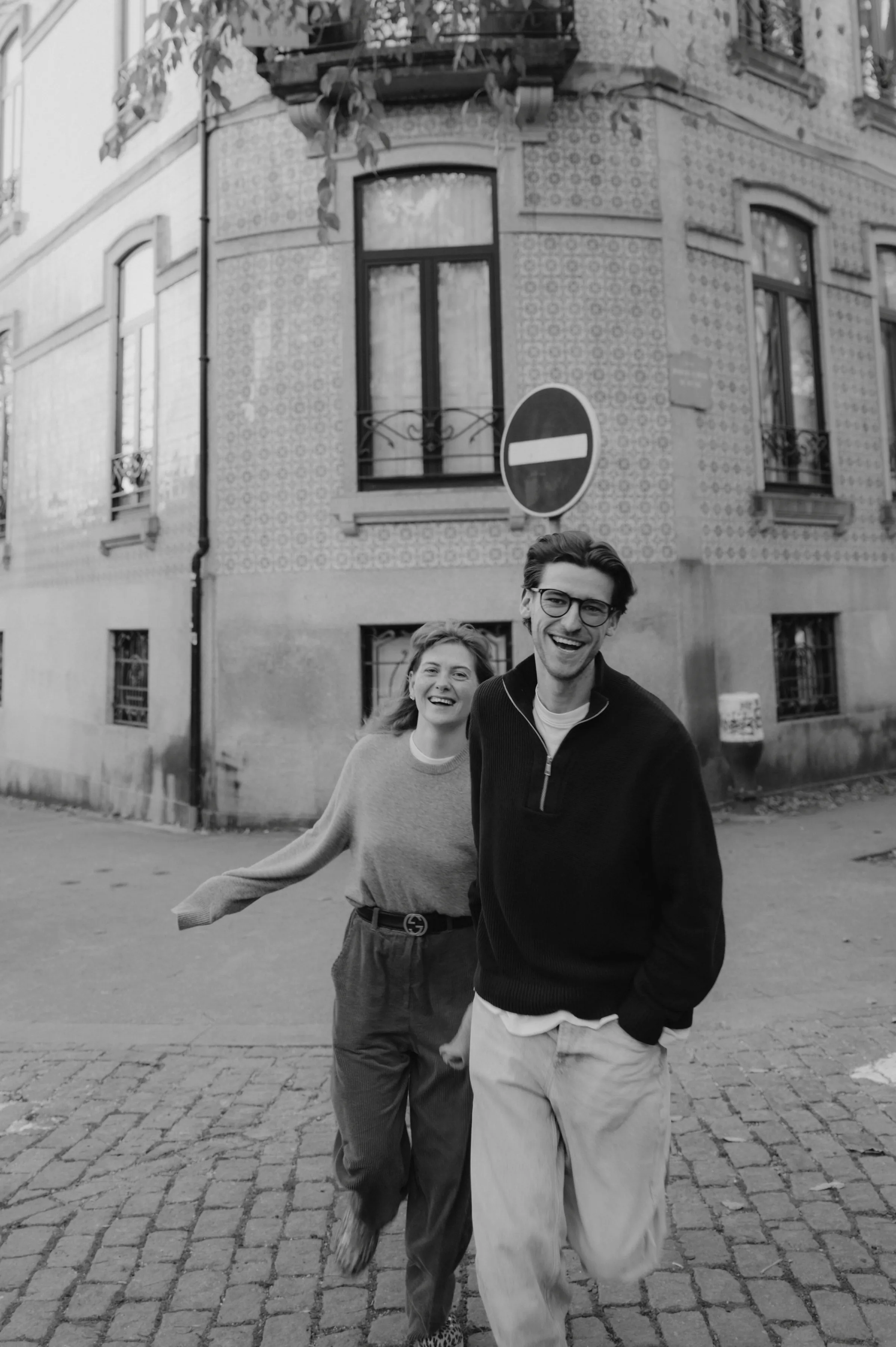 Couple walking on a cobblestone city street during an outdoor session, framed by old building facades.