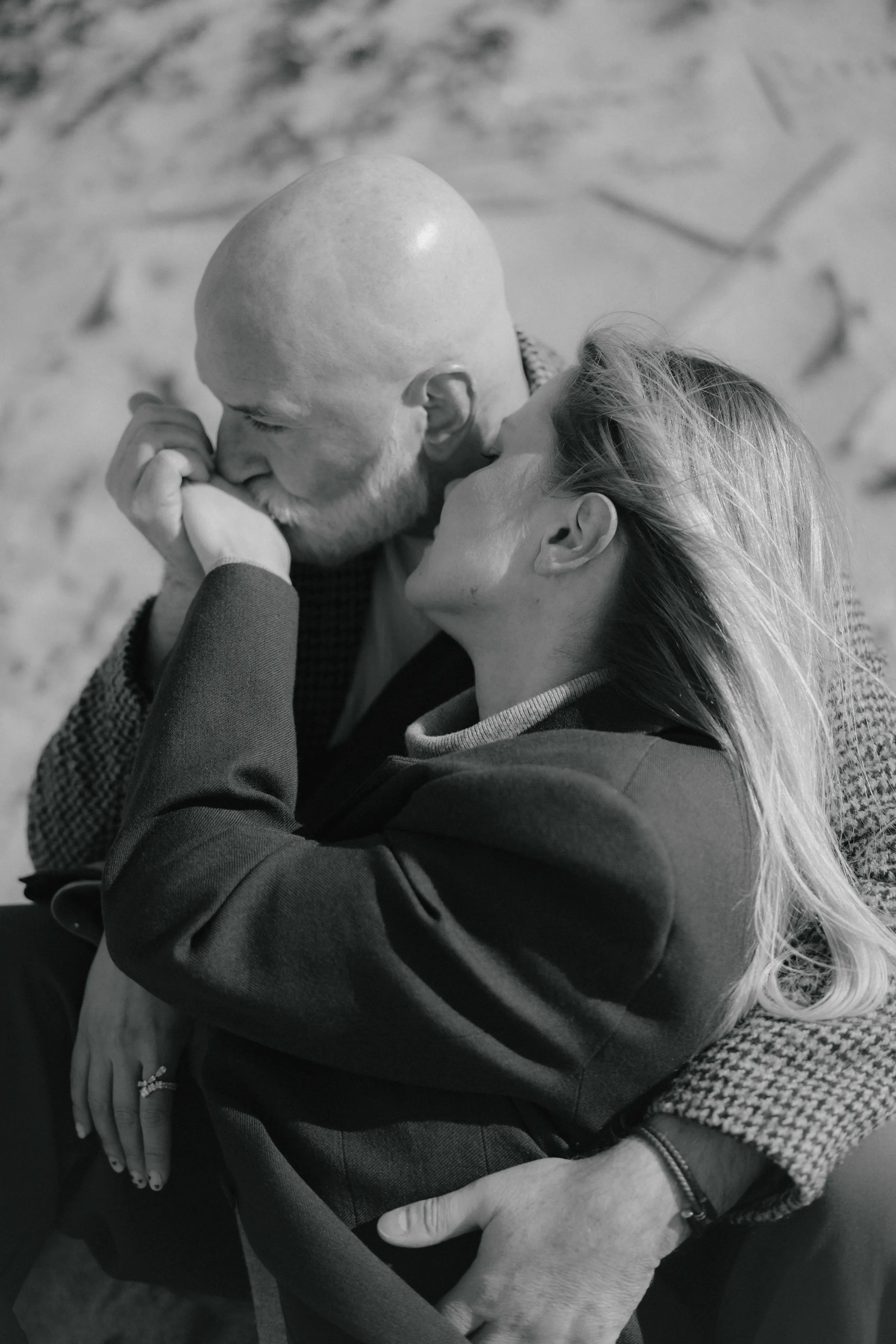 Black-and-white close portrait of a couple seated close together outdoors, sharing a gentle forehead kiss.