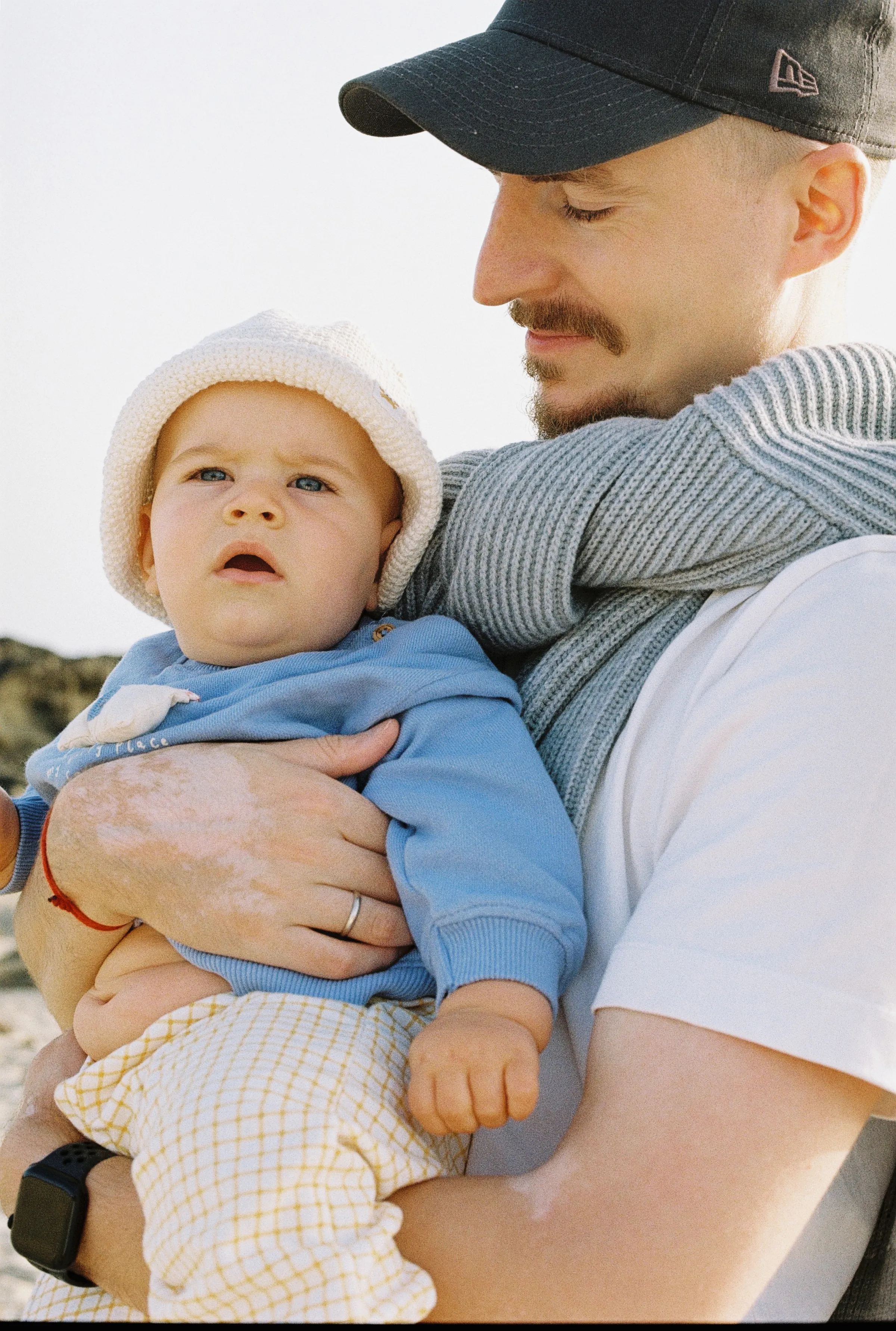 Close outdoor family portrait with an adult holding a baby in soft light.