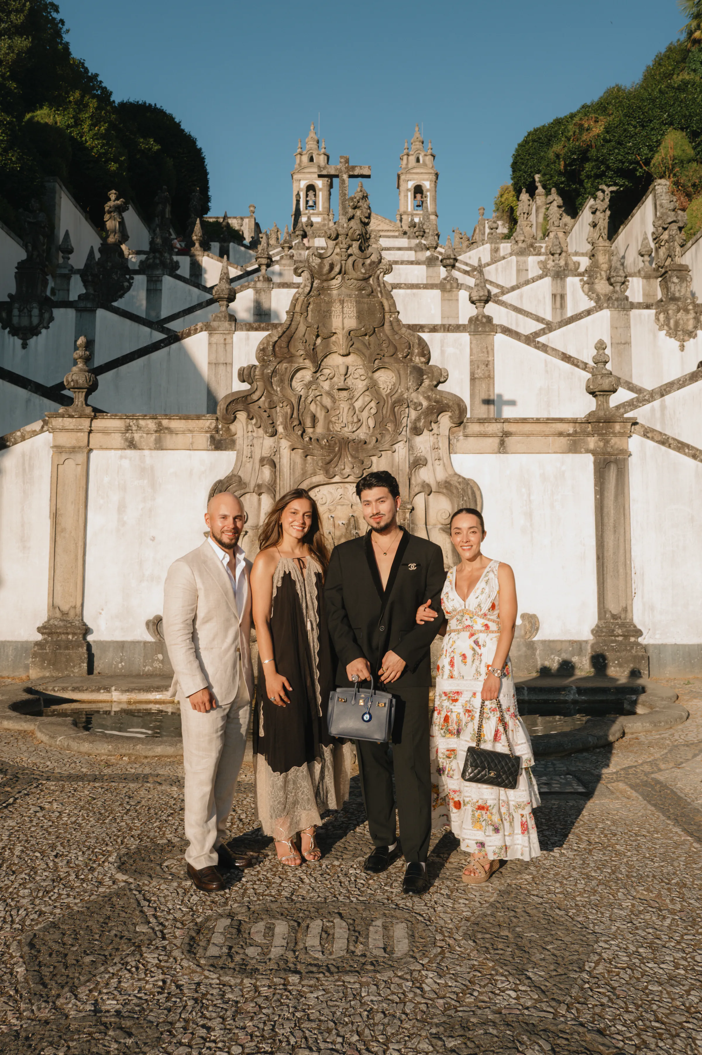 Group portrait of four adults in formal attire outside an ornate stone church staircase.