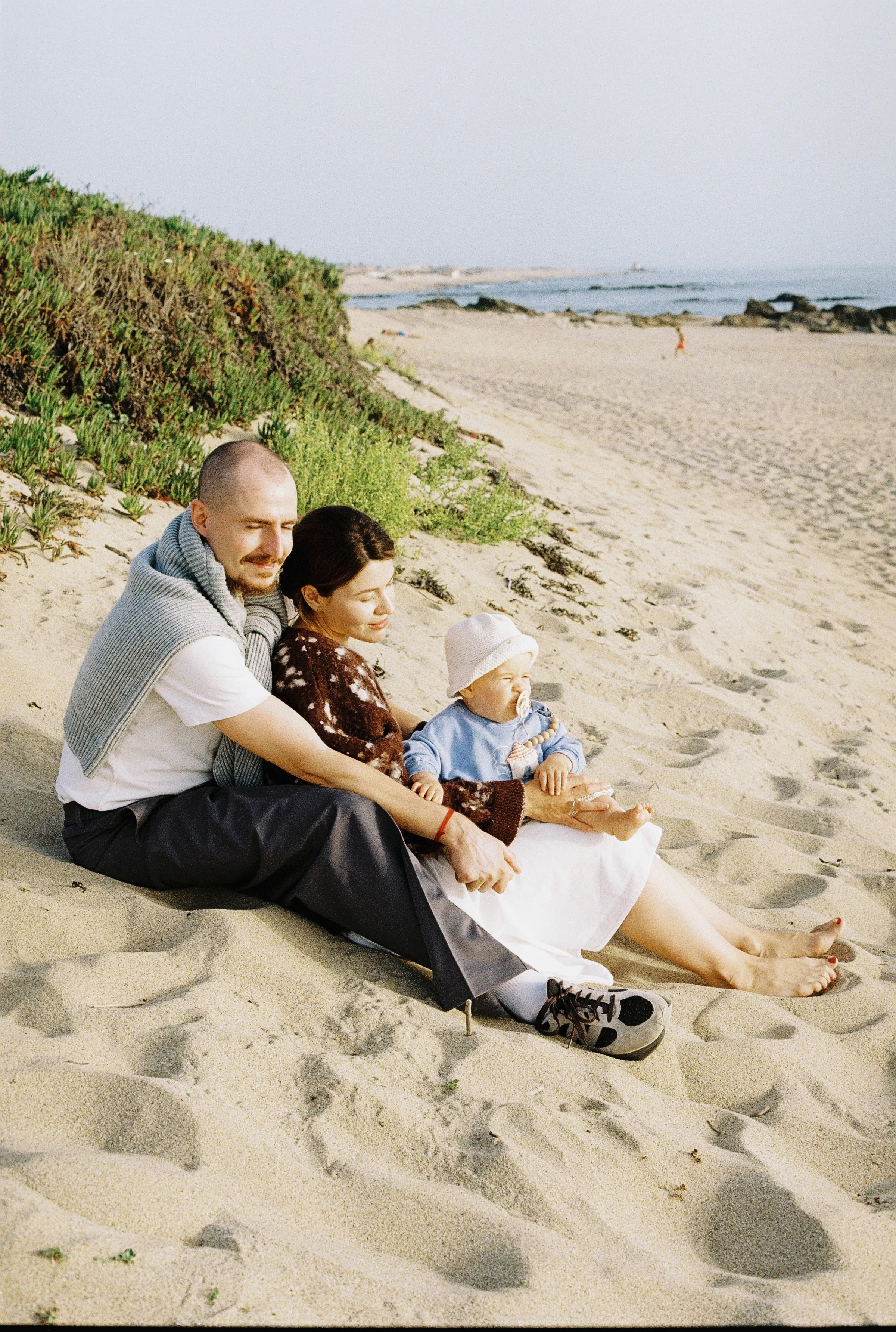 Family seated together on a sandy beach during a seaside outdoor session in soft light