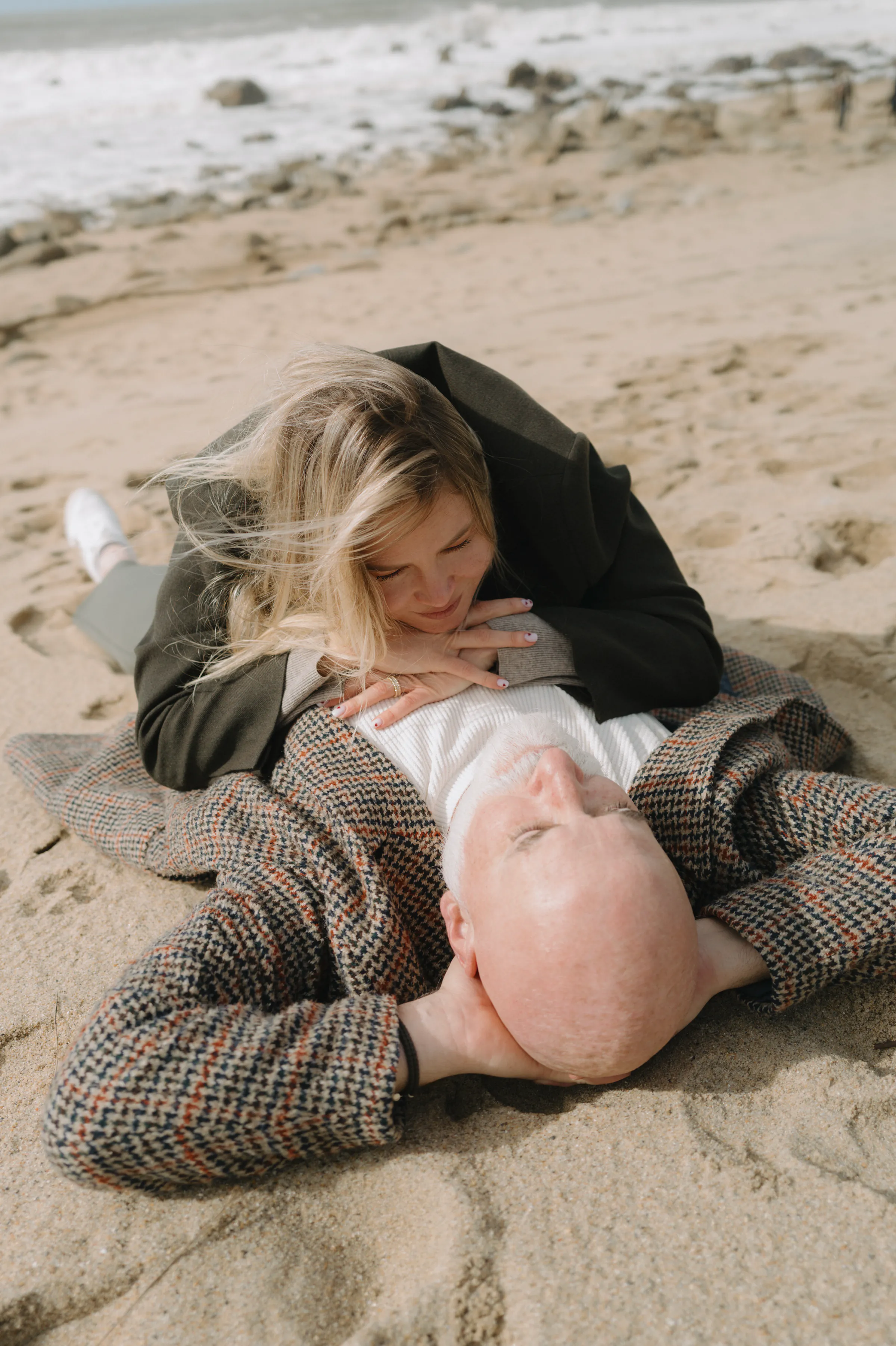 Couple lying close together on a sandy beach during a seaside outdoor session.