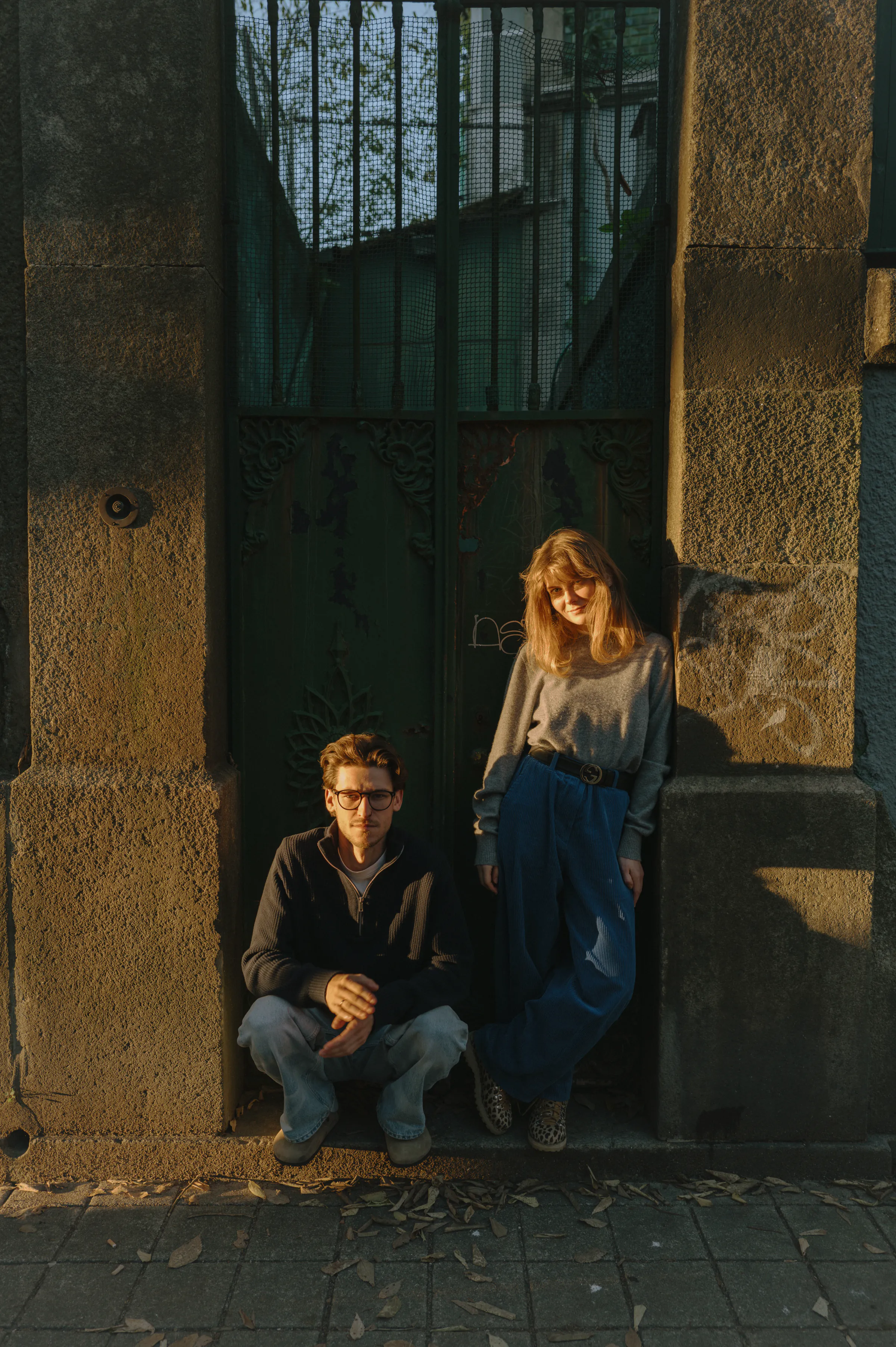 Couple portrait by a stone doorway and tall green gate during a warm city walk session.