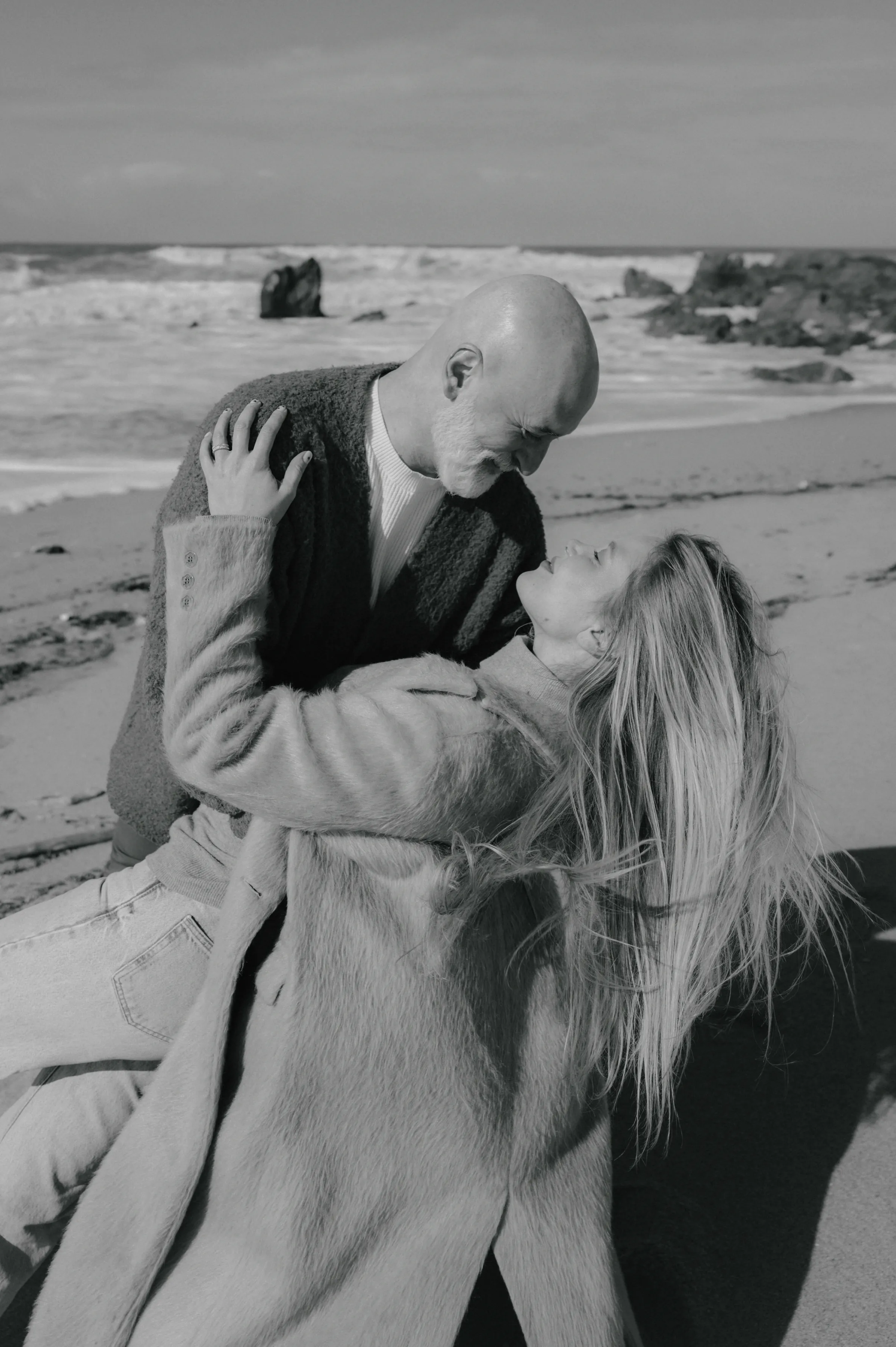 Couple sharing a close kiss during a seaside portrait session, captured in black and white.