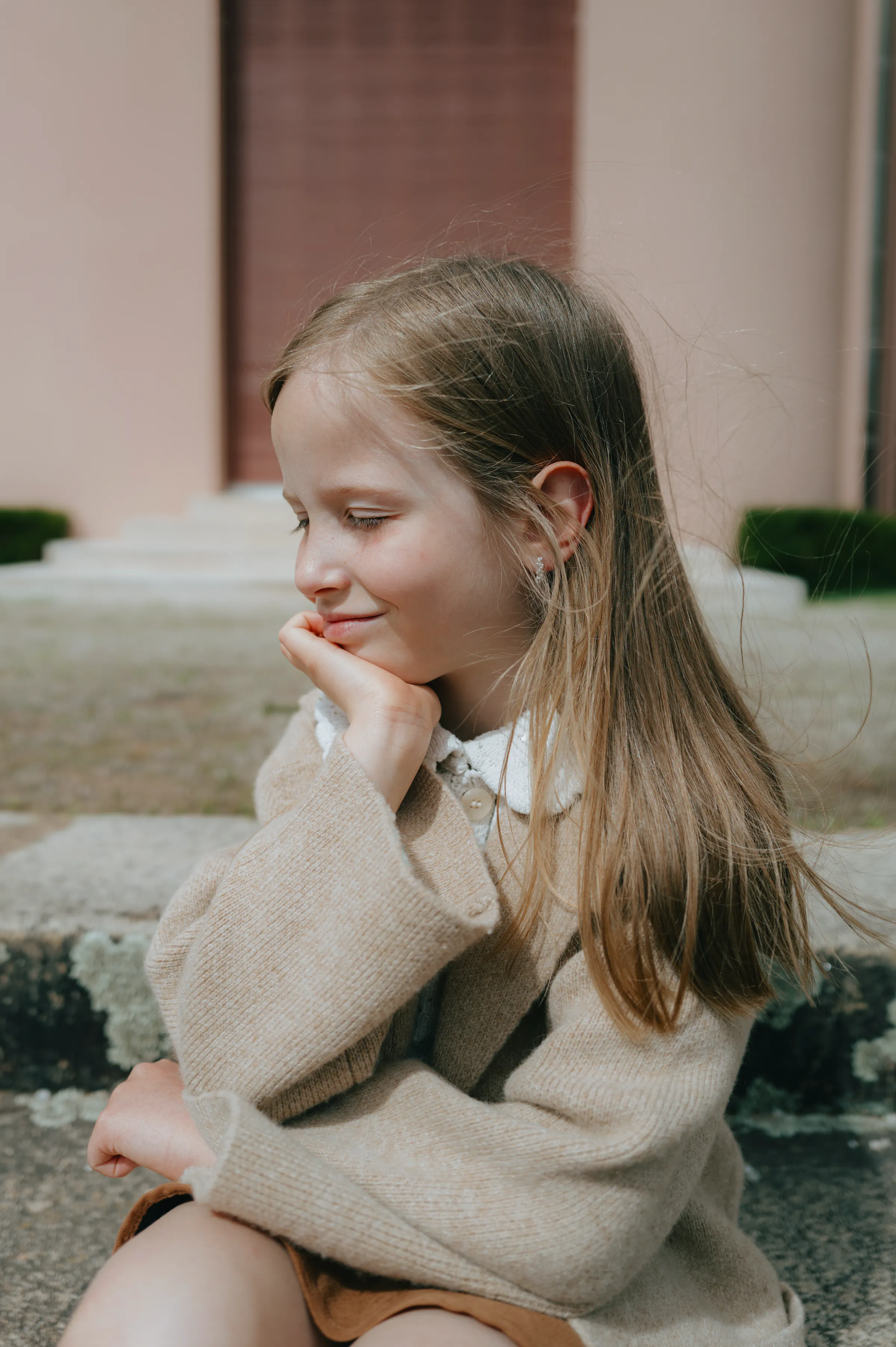 Child portrait on stone steps during an outdoor session, chin resting in soft light.