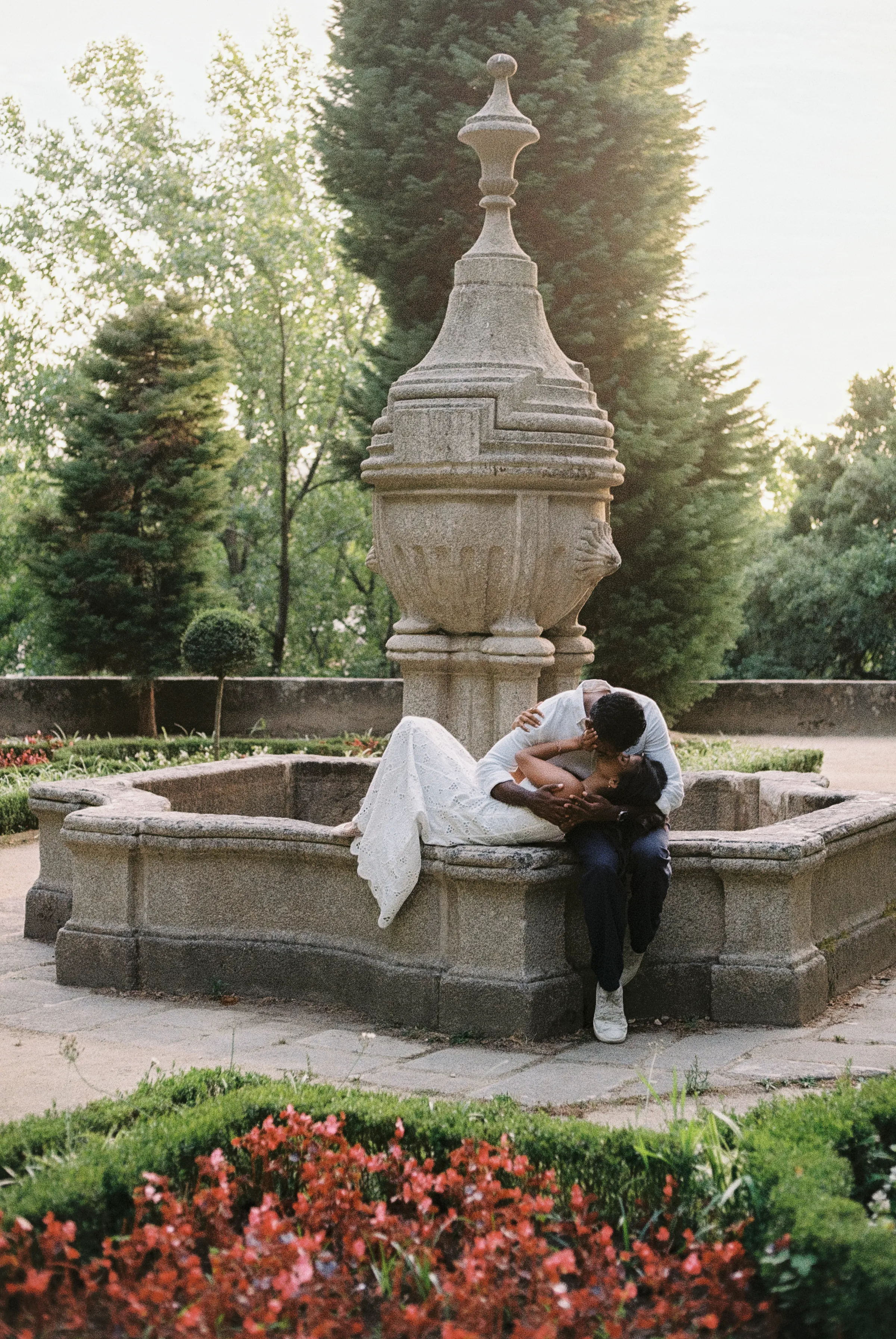 Couple in formal attire sitting by a stone fountain during a garden portrait session.