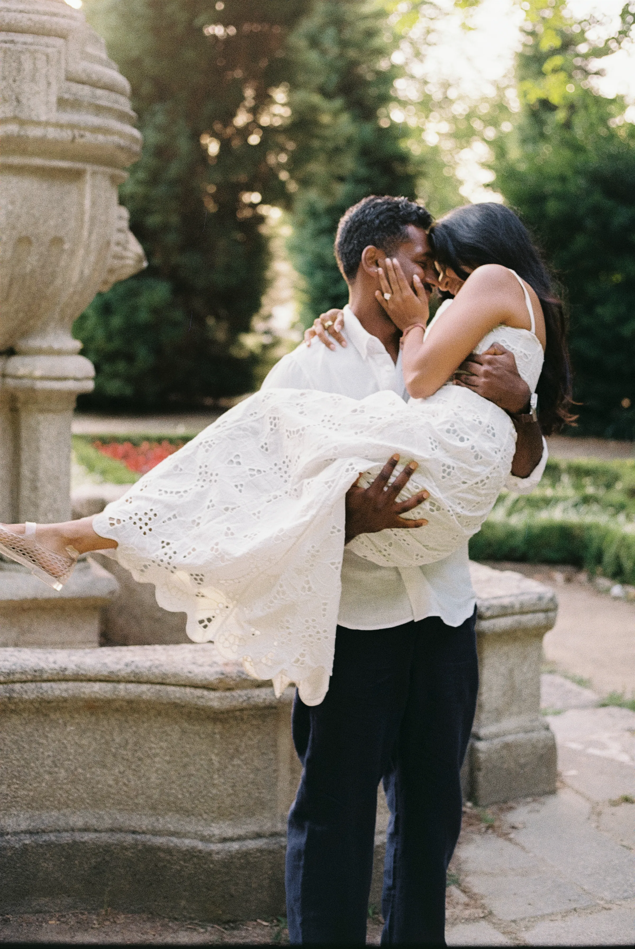 Couple embracing beside a stone fountain during a soft light garden portrait session.