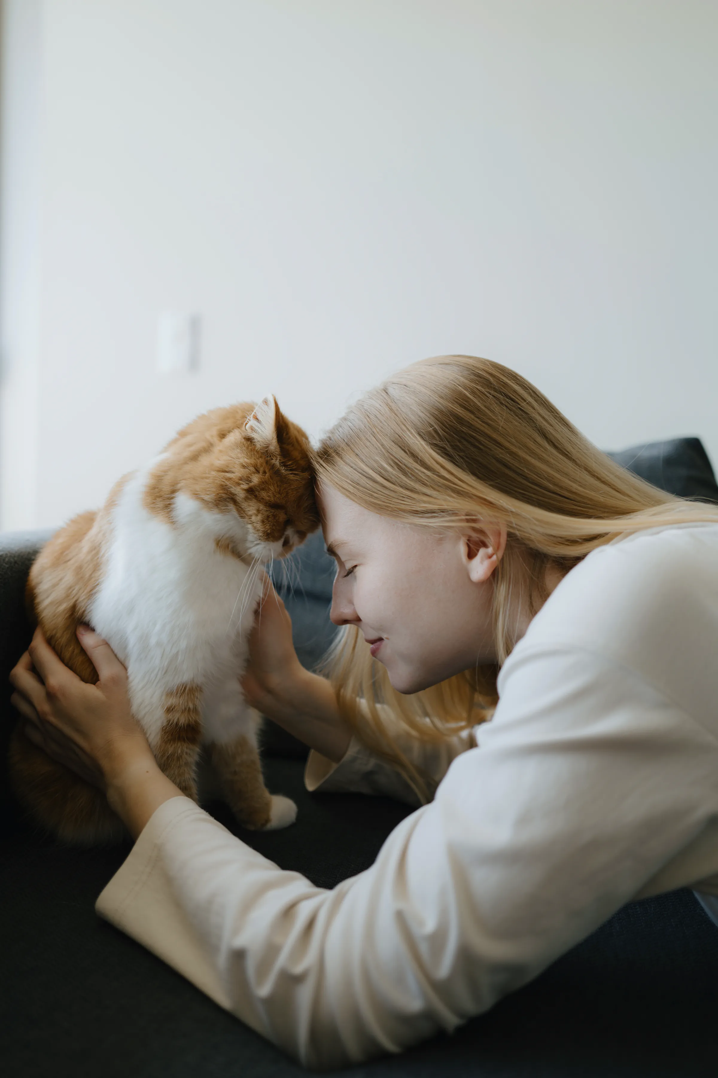 Close indoor portrait of a person gently leaning toward an orange-and-white cat on a sofa.