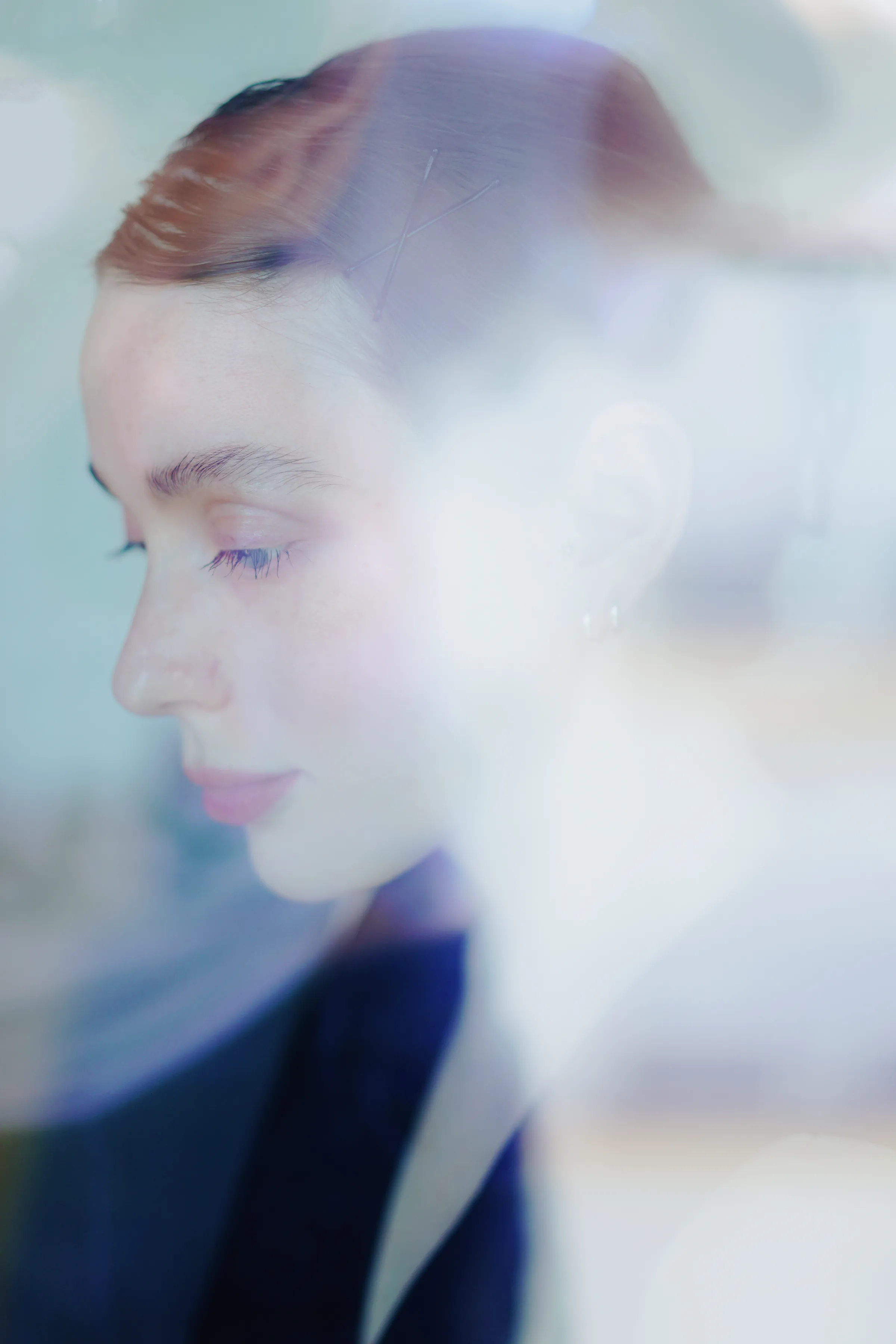 Close portrait of a person in profile through glass, with soft light and layered reflections.