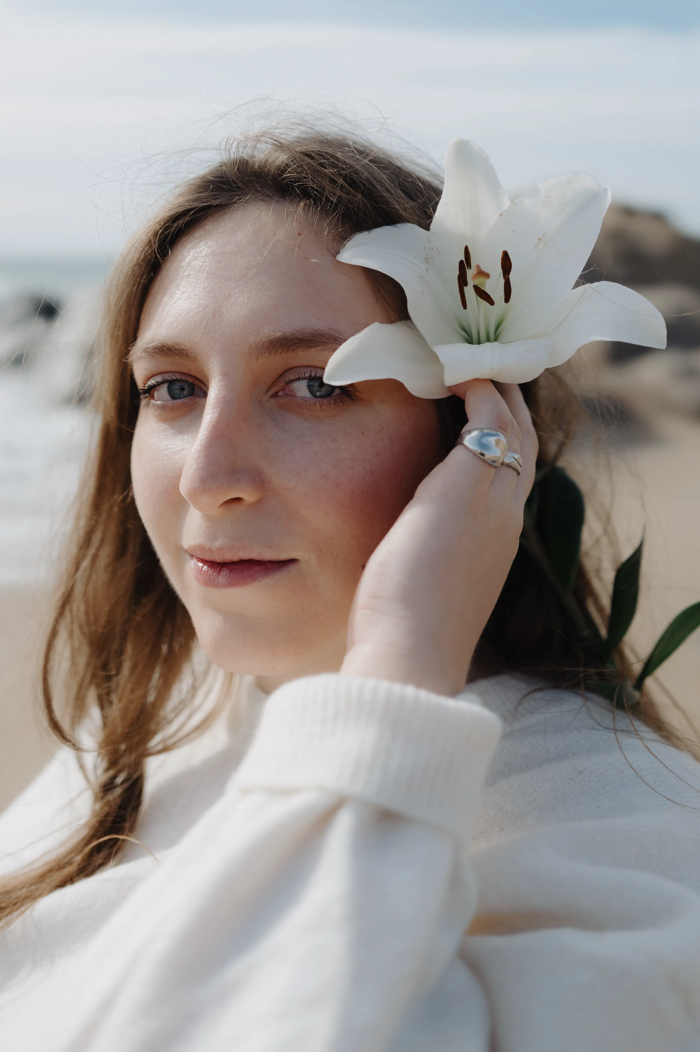 Close seaside portrait of an adult holding a white lily by their face in soft light.