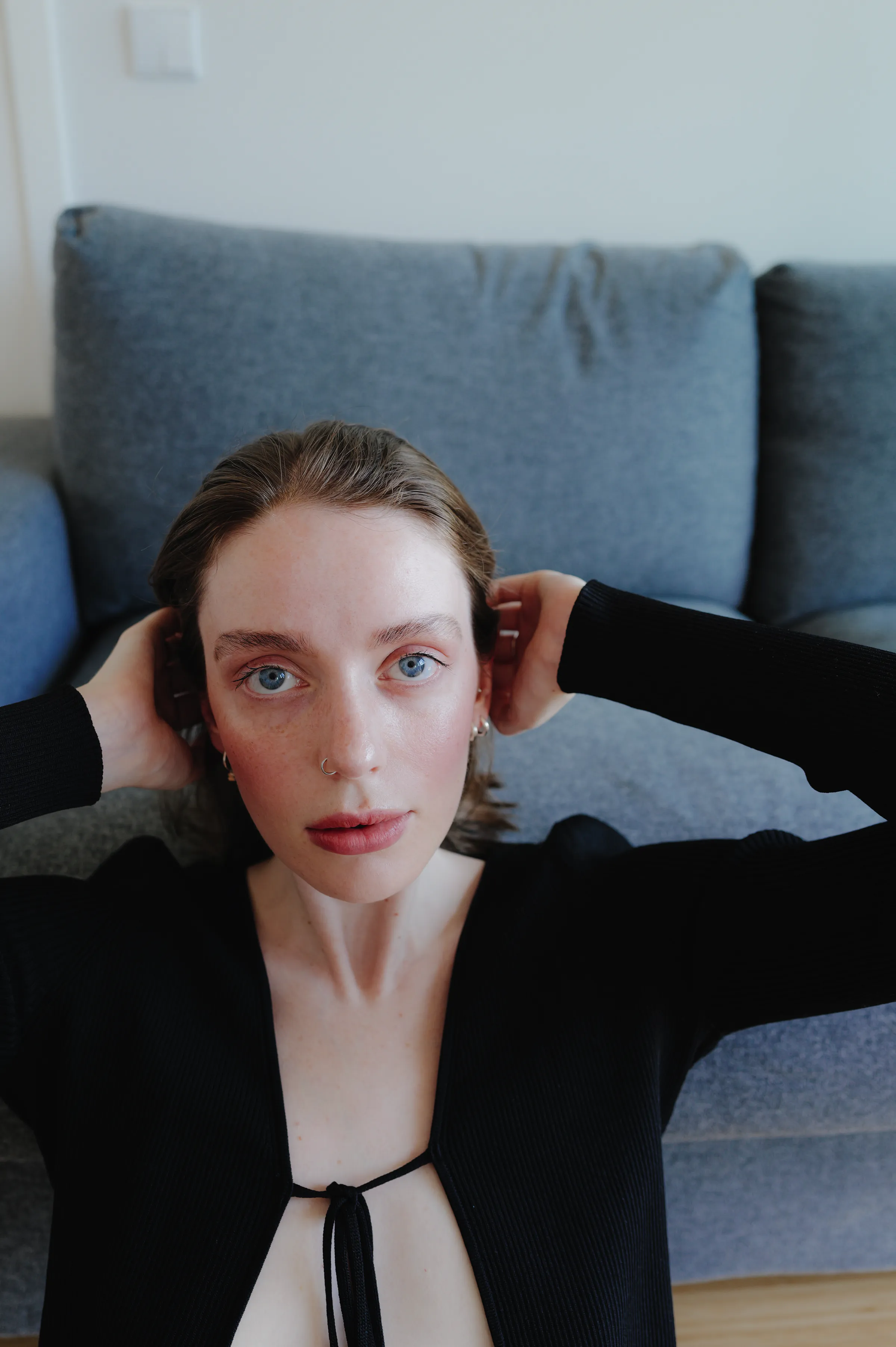 Close portrait of a person in a black top seated on a gray sofa in soft indoor light.
