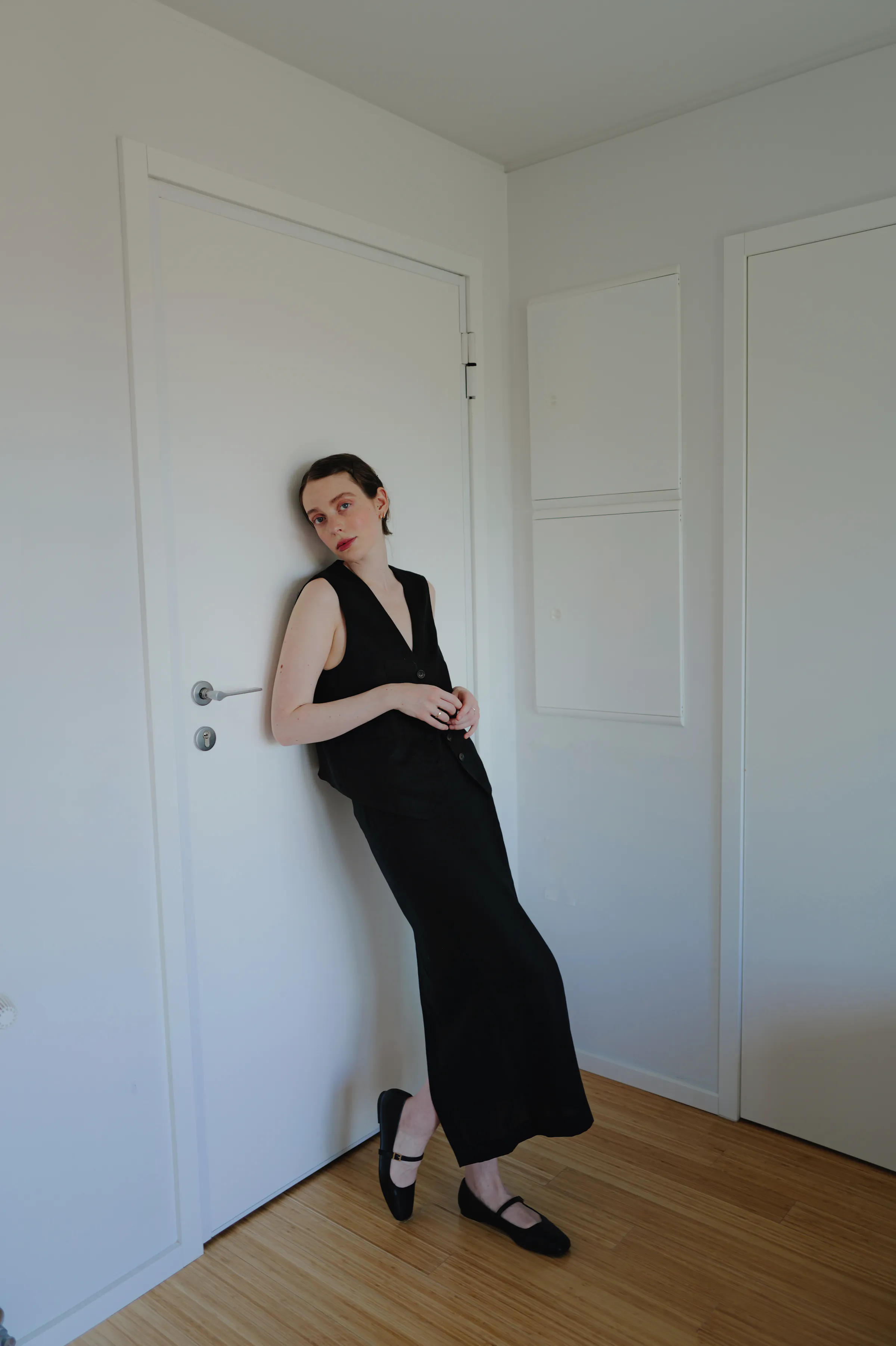 Portrait of a person in a black dress leaning against a white door during a home session.